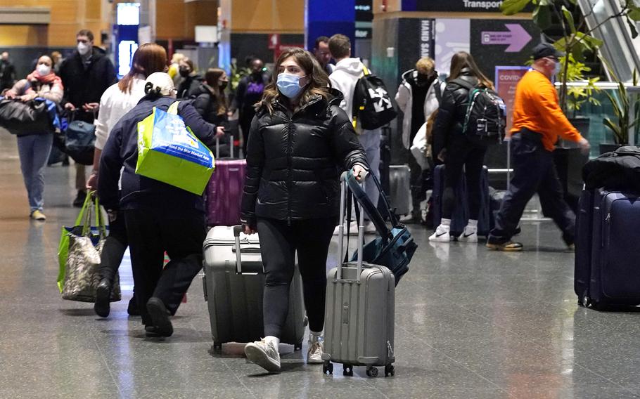 Travelers trek through Terminal E at Logan Airport, Tuesday, Dec. 21, 2021, in Boston.  At least three major airlines say they have canceled dozens of flights, Friday, Dec. 24,  because illnesses largely tied to the omicron variant of COVID-19 have taken a toll on flight crew numbers during the busy holiday travel season.  