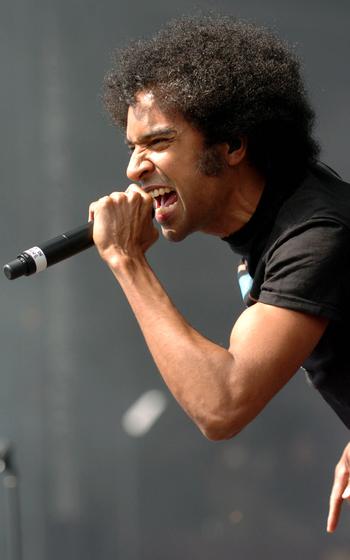 A man leans forward and sings while gripping a microphone with one hand.
