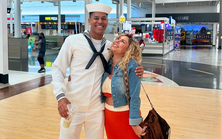 A sailor in white uniform poses with is arm around a woman wearing a blue jacket.