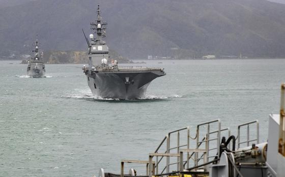 Two ships approach a port; mountains are in the background.