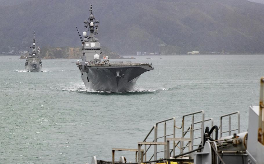 Two ships approach a port; mountains are in the background.
