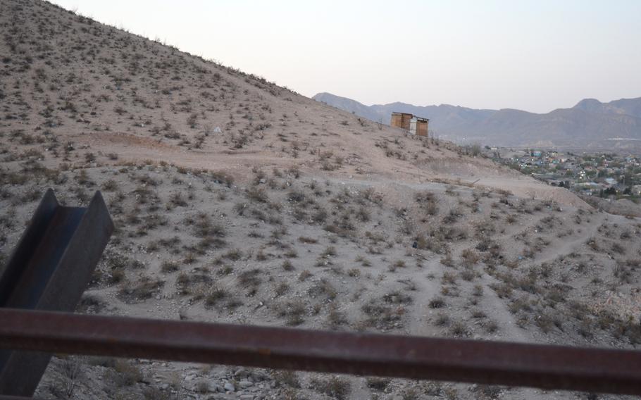 A wooden structure on the side of a hill in the desert with a town in the background. 