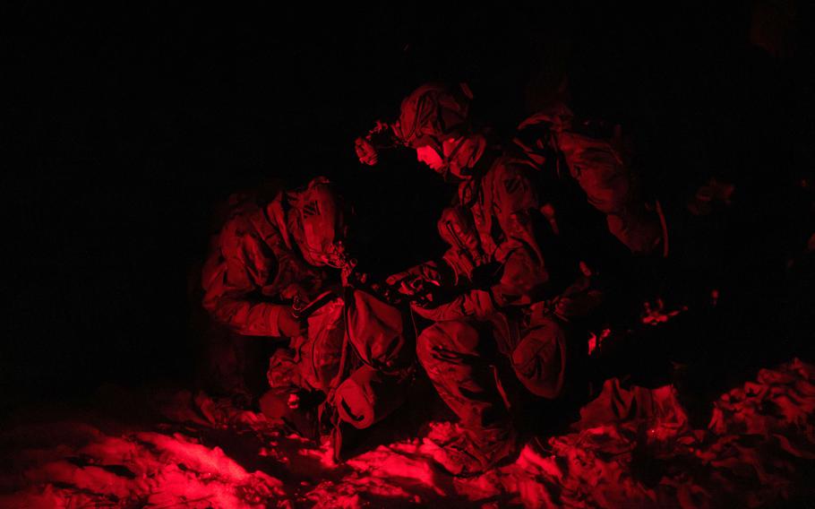 Soldiers training in a nighttime reconnaissance exercise made barely visible by a red light.