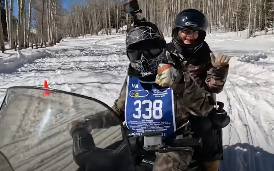 Two people wave as they sled down a snowy hill