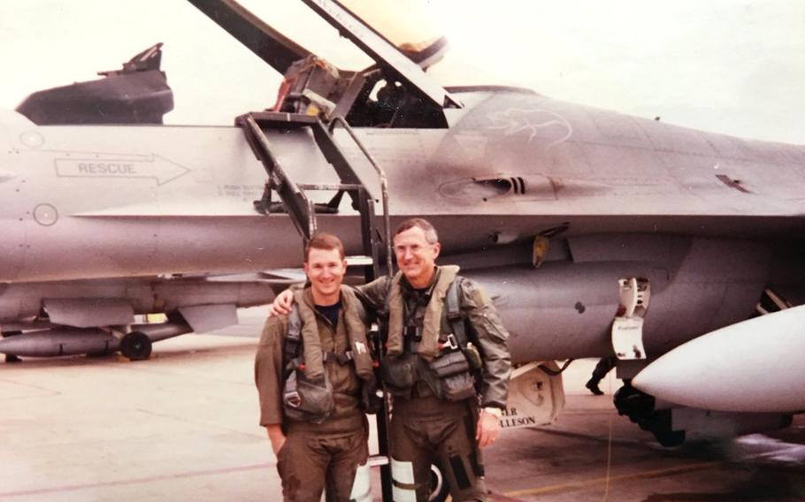 Two pilots, a father and son, pose for a photo in front of a fighter jet.