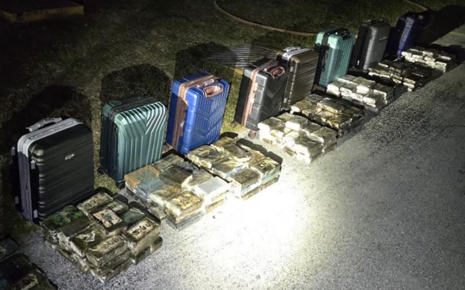 Open suitcases displaying packages of cocaine sit on the ground illuminated by a light in the dark.