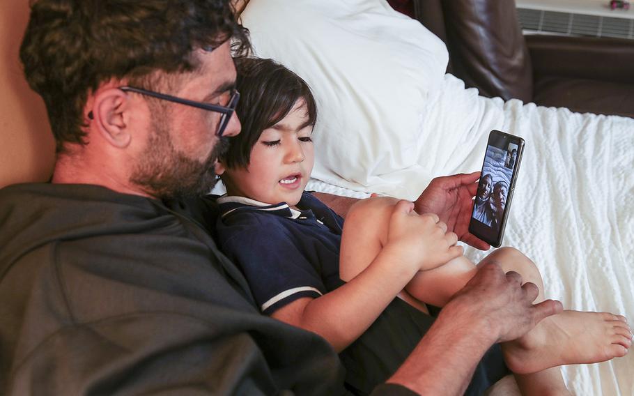 Zabih Khan holds a phone as his 4-year-old brother Mojib talks about a knee scratch he got while playing during a video call with their parents in Afghanistan. 