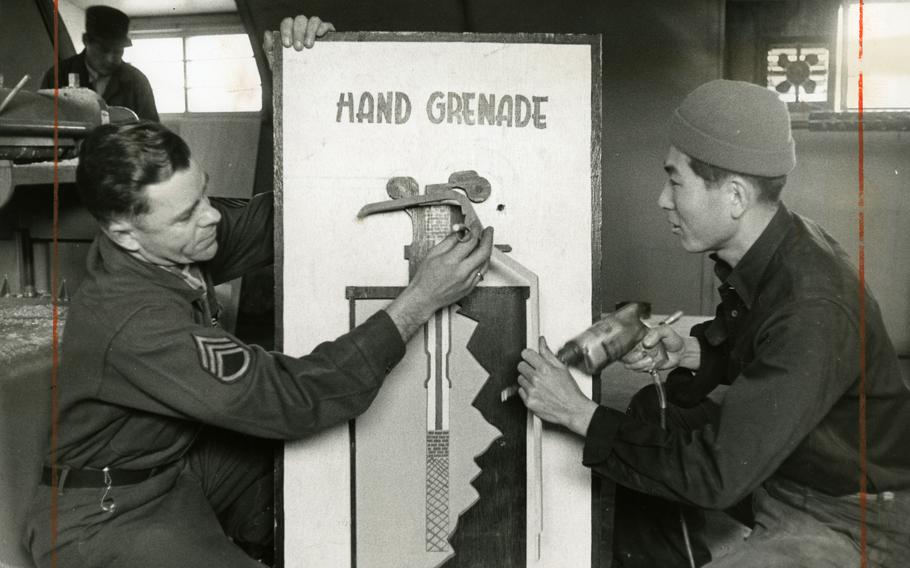 A black and white photo of two men next to a poster.