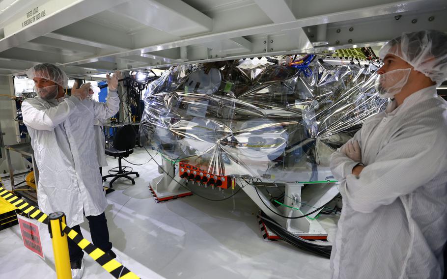 Orion program engineers talk in front of the Artemis II crew capsule being assembled at Kennedy Space Center, Fla., on Sunday, Aug. 28, 2022. The capsule will carry astronauts on a mission to orbit the moon in the future.