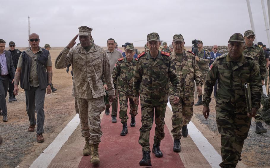 Langley, walking with Berrid and a group of military people and civilians, salutes.