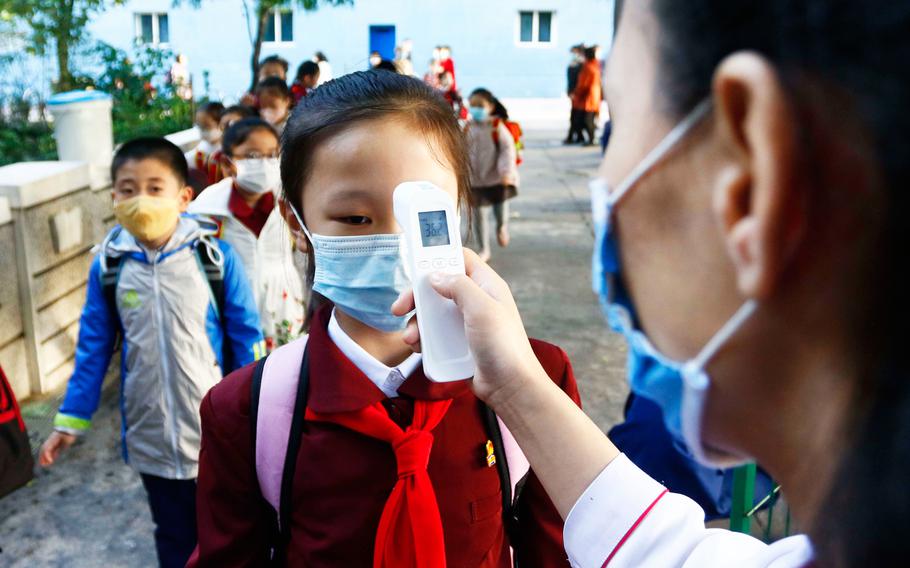 A teacher takes the body temperature of a schoolgirl to help curb the spread of the coronavirus before entering Kim Song Ju Primary School in Central District in Pyongyang, North Korea.