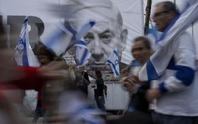 Demonstrators walk with Israel's national flags next to a banner showing Prime Minister Benjamin Netanyahu during a protest against plans by his government to overhaul the judicial system in Tel Aviv, Israel, Saturday, March 25, 2023. (AP Photo/Oded Balilty)