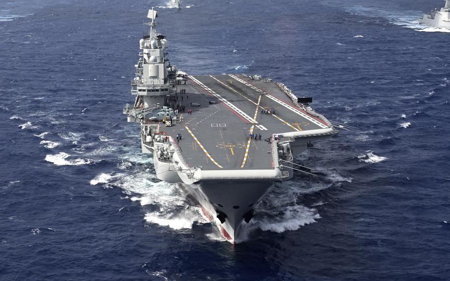 An aircraft carrier, seen from the front, sails in open ocean.