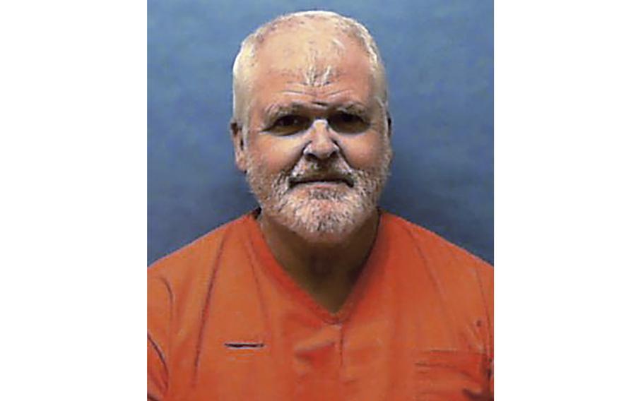 A man in an orange jumpsuit against a blue wall.