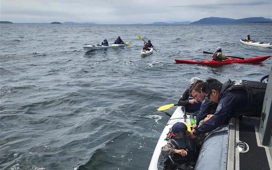 Rescue personnel help a kayaker out of the water and into a boat.