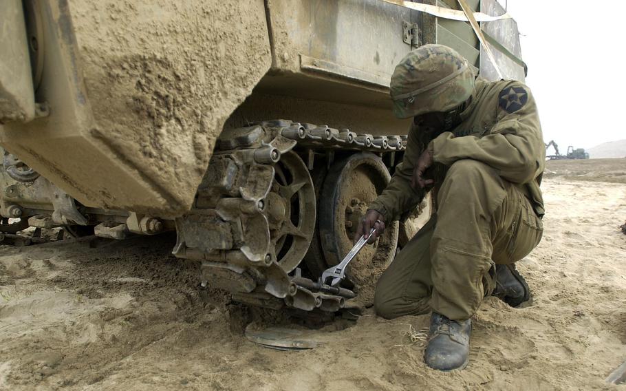 A soldier holding a wrench kneels by an armored vehicle.