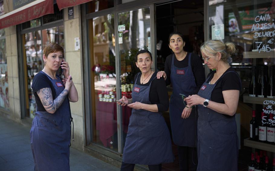 Vendors wearing blue aprons step outside a shop as they react to a power outage in Barcelona.