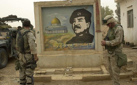 Marines stand at the gate of a suspected terrorist training camp outside of Baghdad, Iraq, with a mural of Saddam Hussein, April 7, 2003. Twenty years later, Iran maintains considerable influence over Iraq, and the U.S. still has troops in the country to prevent an Islamic State group resurgence.
