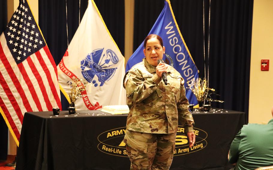 A woman in uniform speaks into a microphone in front of a table covered with a black cloth.
