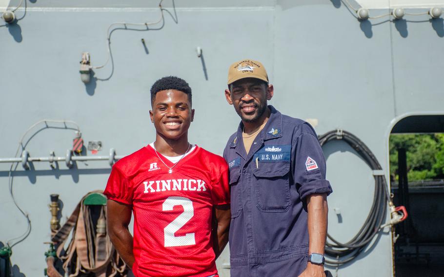 A member of the Nile C. Kinnick High School football team poses with his father aboard the aircraft carrier USS Ronald Reagan at Yokosuka Naval Base, Japan, Tuesday, Sept. 12, 2023.