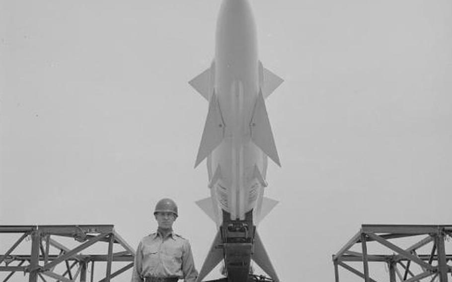 A soldier stands at attention in front of a Nike missile in May 1955.
