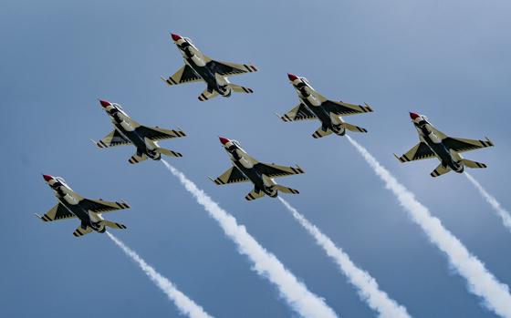 Six military fighter jets, seen from below, fly in a triangular formation emitting smoke from their tails during an air show.