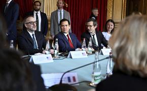 Marco Rubio in the center of a photo, sitting at a table with other people in suits on either side of him.
