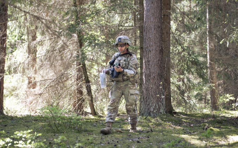 One soldier in a forested area, with trees behind her.