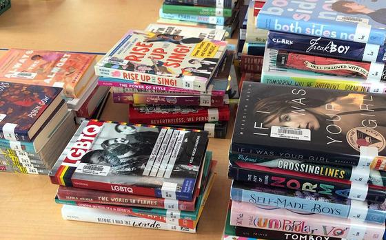 Books that were temporarily removed in February for a compliance review are stacked up on a table in the library at Ramstein High School in Germany. The American Civil Liberties Union is suing the Department of Defense Education Activity on behalf of 12 students, arguing that DODEA's removals of books and curriculum violate their First Amendment rights.