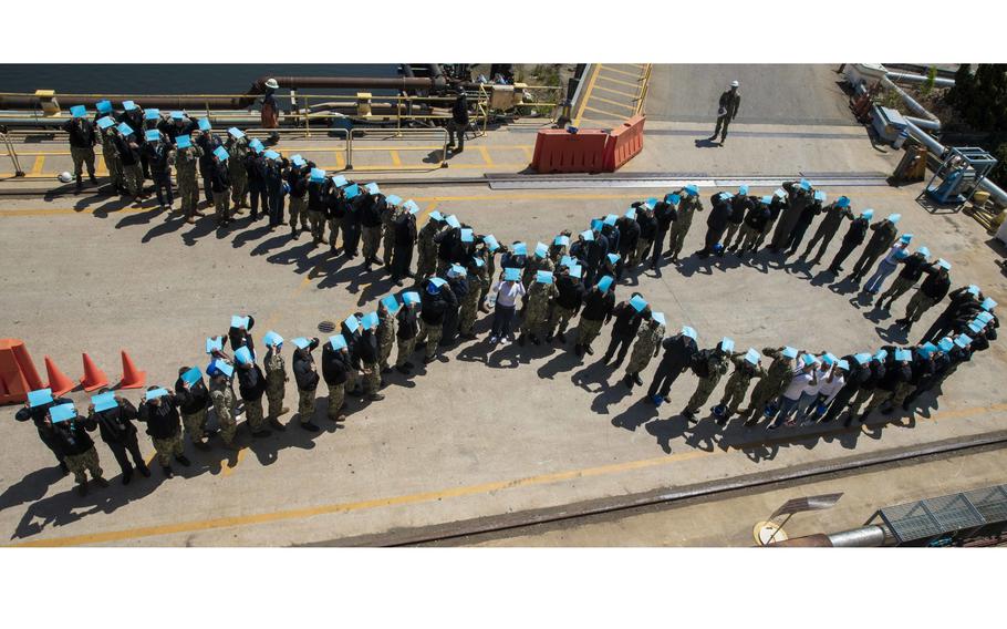 Sailors assigned to the amphibious assault ship USS Wasp pose in April 2022 in Norfolk, Va., for a photo on a pier at BAE Systems Shipyard. Sailors stood in the shape a ribbon while holding teal paper to show support for sexual assault victims.