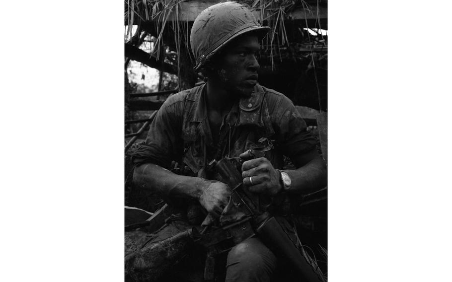 A vertical, black and white photo of a soldier holding a partially dismantled rifle.