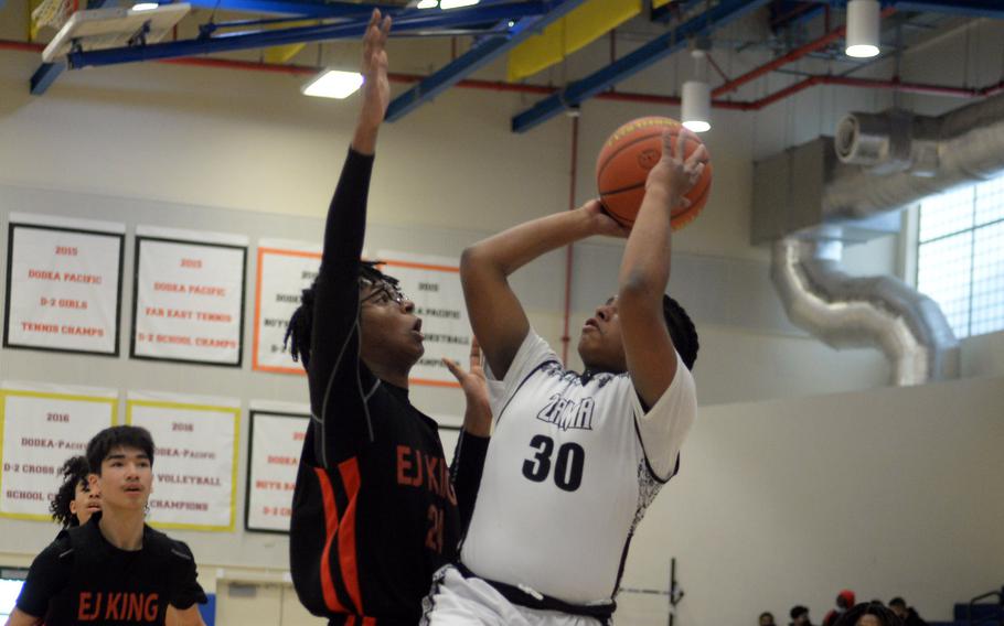 Zama‘s Amari King shoots against E.J. King’s Keith Lombard during Thursday’s DODEA-Japan boys basketball tournament game. The Trojans won 65-56.