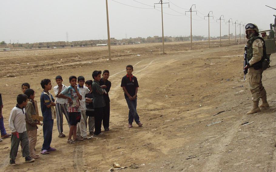 A soldier with a rifle near a gaggle of children in the desert.