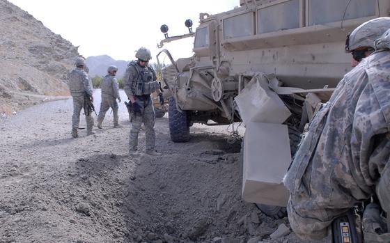 Troops survey a hole in the ground next to an armored vehicle.