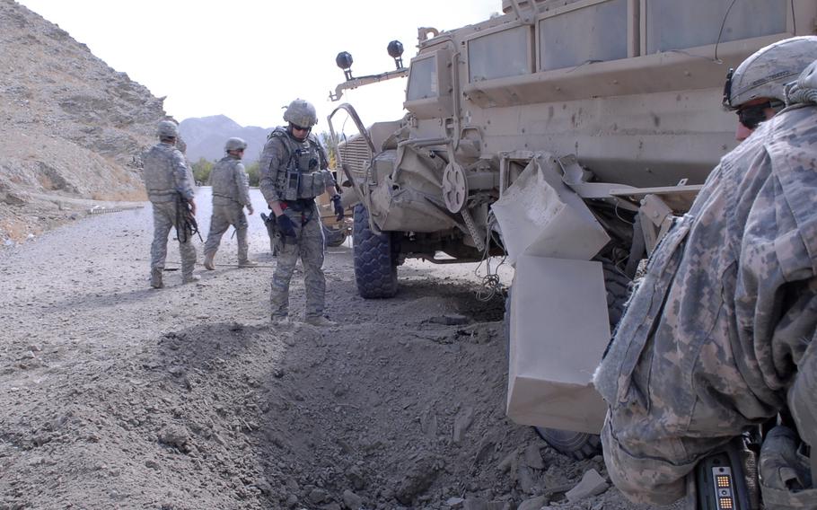 Troops survey a hole in the ground next to an armored vehicle.