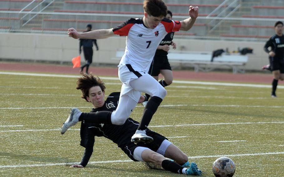 Nile C. Kinnick’s Kou Nishiyama leaps over the slide tackle of Zama’s Pierce Ingram during Friday’s Perry Cup soccer matches. The Red Devils won 4-0.