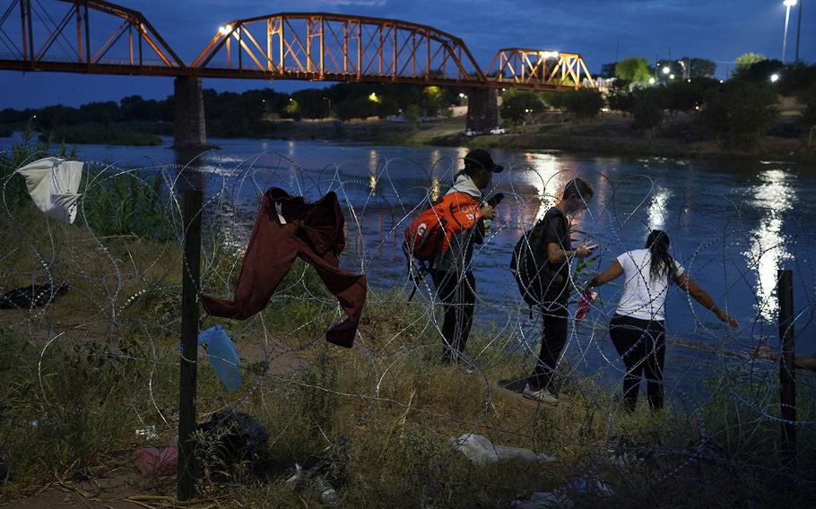 Migrants walk along the Rio Grande in the United States near the Eagle Pass-Piedras Negras International Bridge minutes after wading across the river from Mexico. They later turned themselves into Border Patrol and were transported to a nearby government processing center. 