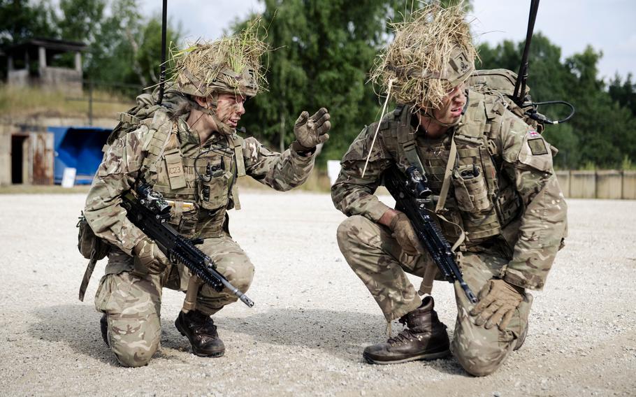 Two Biritish cadets kneel on the ground while discussing infantry tactics.