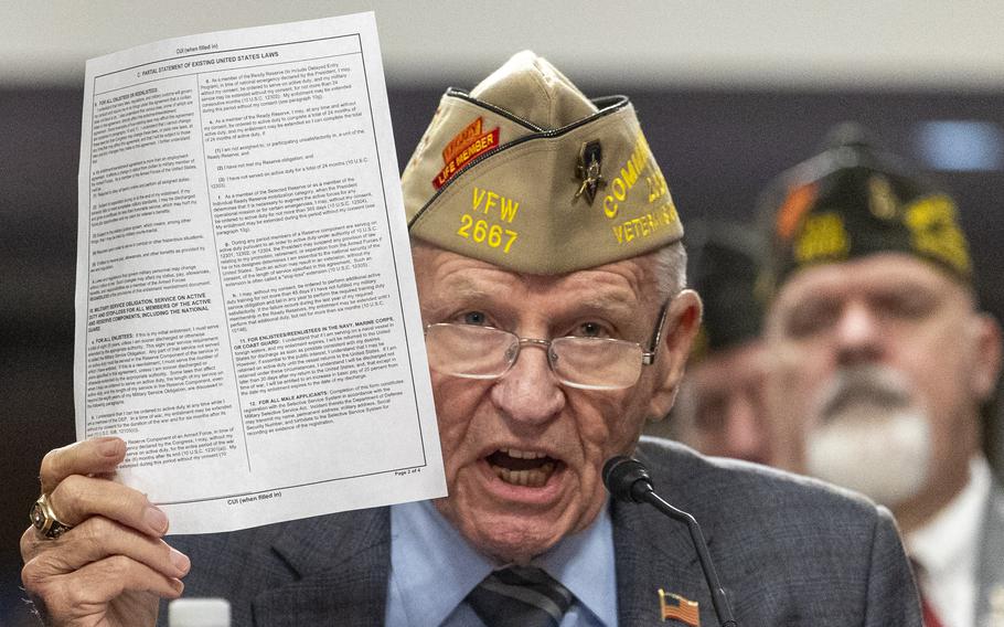 A man in a veterans hat holds up a document.