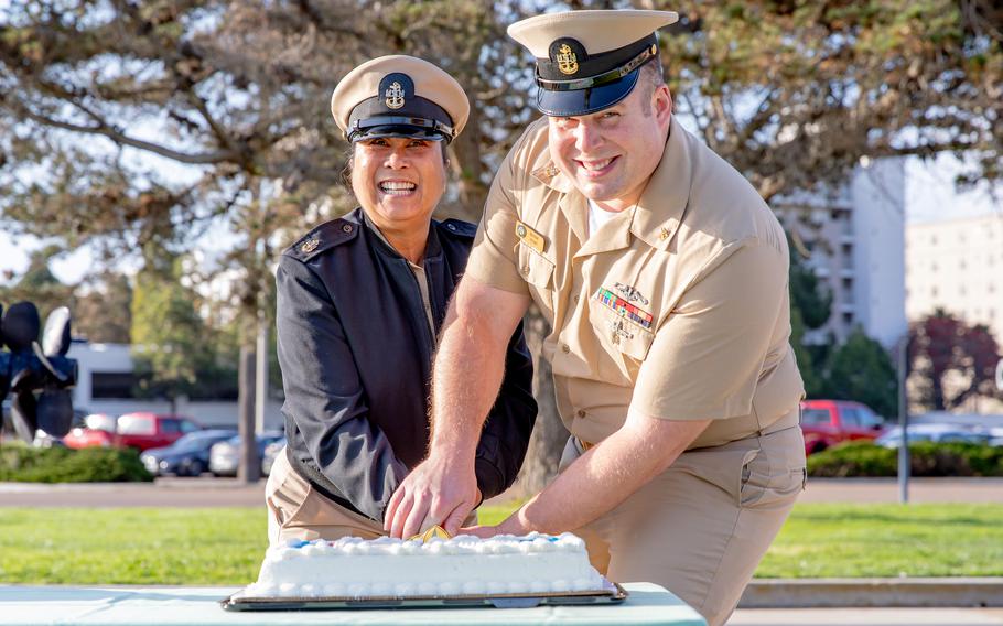 Two sailors cut a cake together while smiling