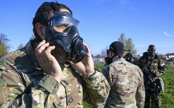 A soldier adjusts a gas mask that he is wearing during training with other troops in the background.