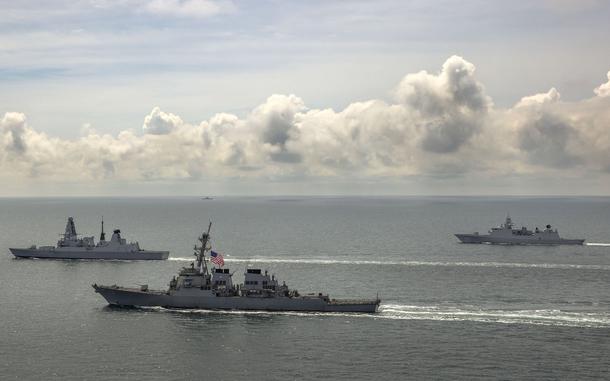 The destroyer USS Laboon, center, the U.K. Royal Navy's HMS Defender, left, and the Dutch HMNLS Evertsen sail together as a Russian warship watches from afar in the Black Sea in June 2021.

