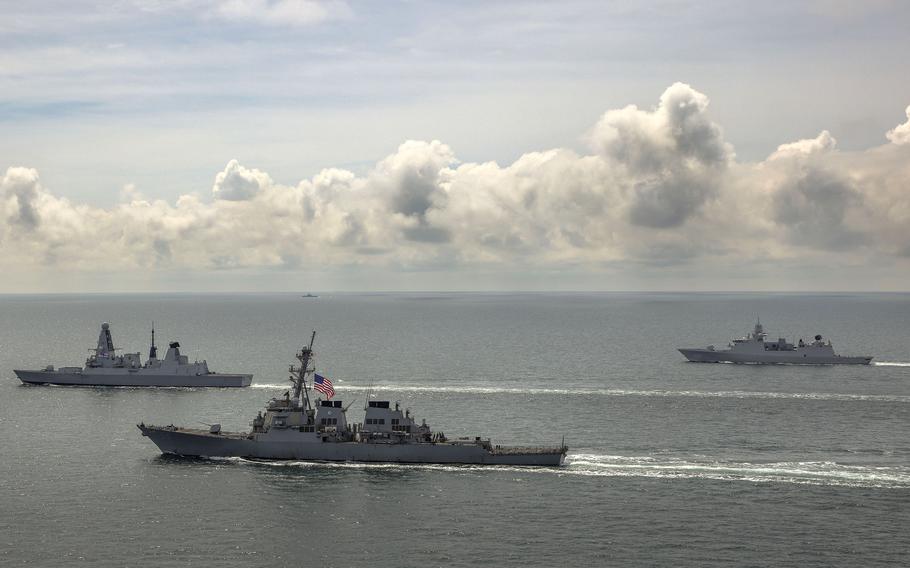 The destroyer USS Laboon, center, the U.K. Royal Navy's HMS Defender, left, and the Dutch HMNLS Evertsen sail together as a Russian warship watches from afar in the Black Sea in June 2021.