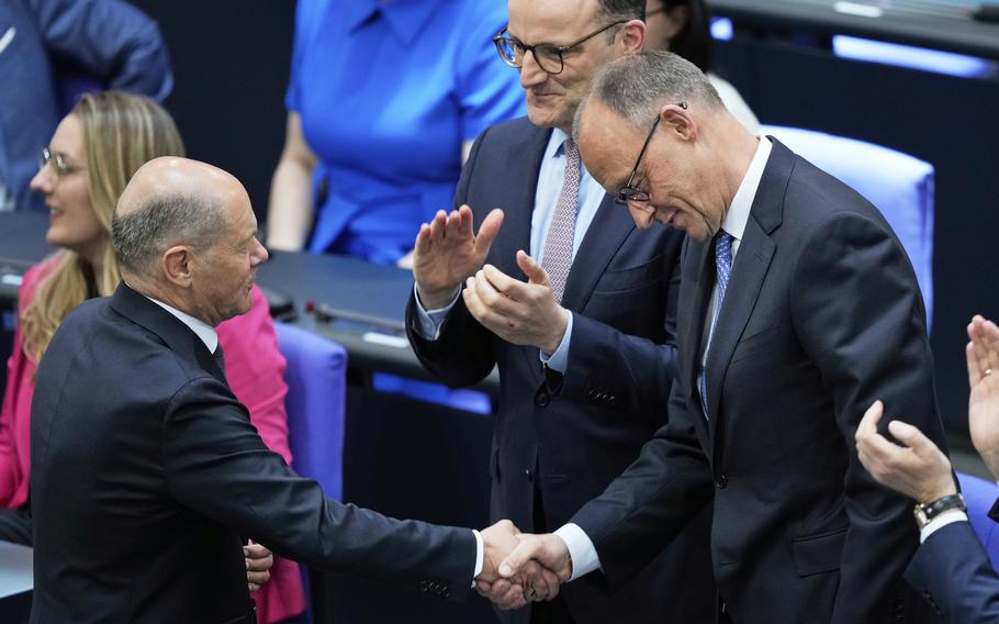 Two men in suits shake hands, with one on the right bowing his head slightly.