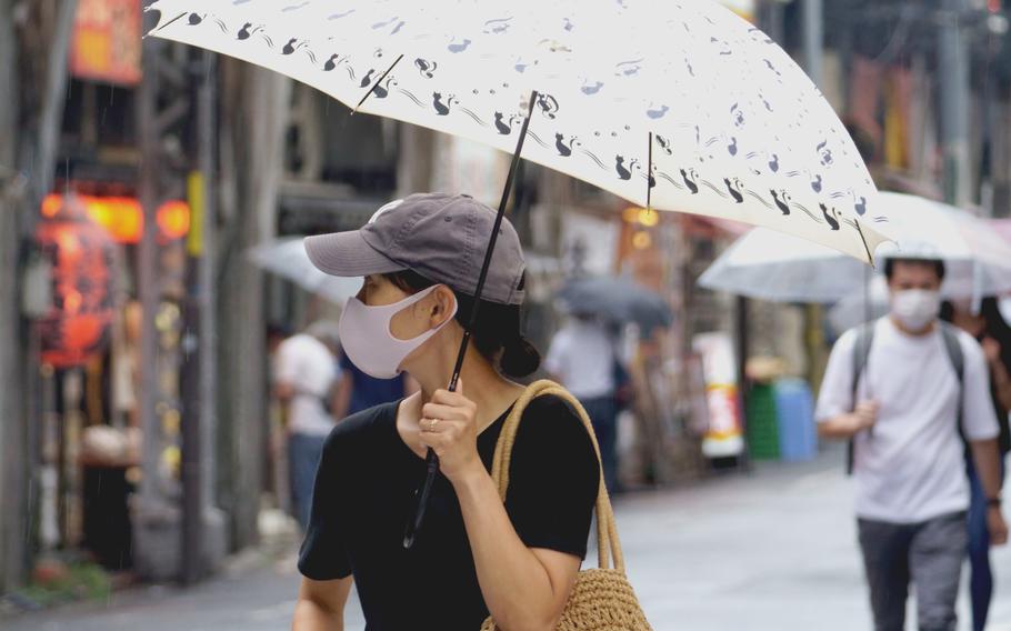 A woman in central Tokyo wears a mask against the coronavirus and carries an umbrella against the rain on Aug. 13, 2021. 