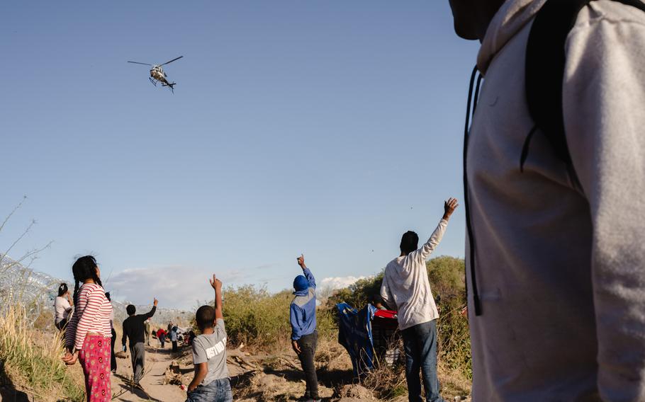 Migrants wave to a Texas Department of Public Safety helicopter after crossing the U.S.-Mexico border through the Rio Grande in El Paso, Texas, on Tuesday, April 2, 2024.