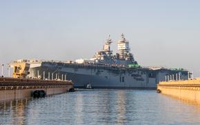 A warship at a dock, with two piers in the foreground partially obscuring either end of it.