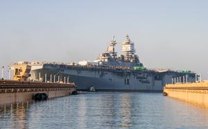 A warship at a dock, with two piers in the foreground partially obscuring either end of it.
