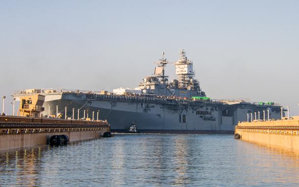 A warship at a dock, with two piers in the foreground partially obscuring either end of it.