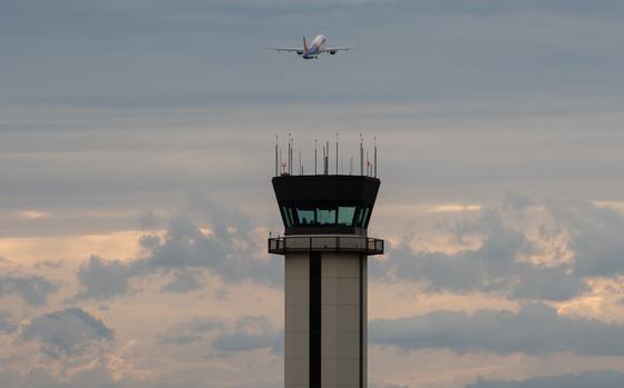 A plane flies away, above an air traffic control tower.